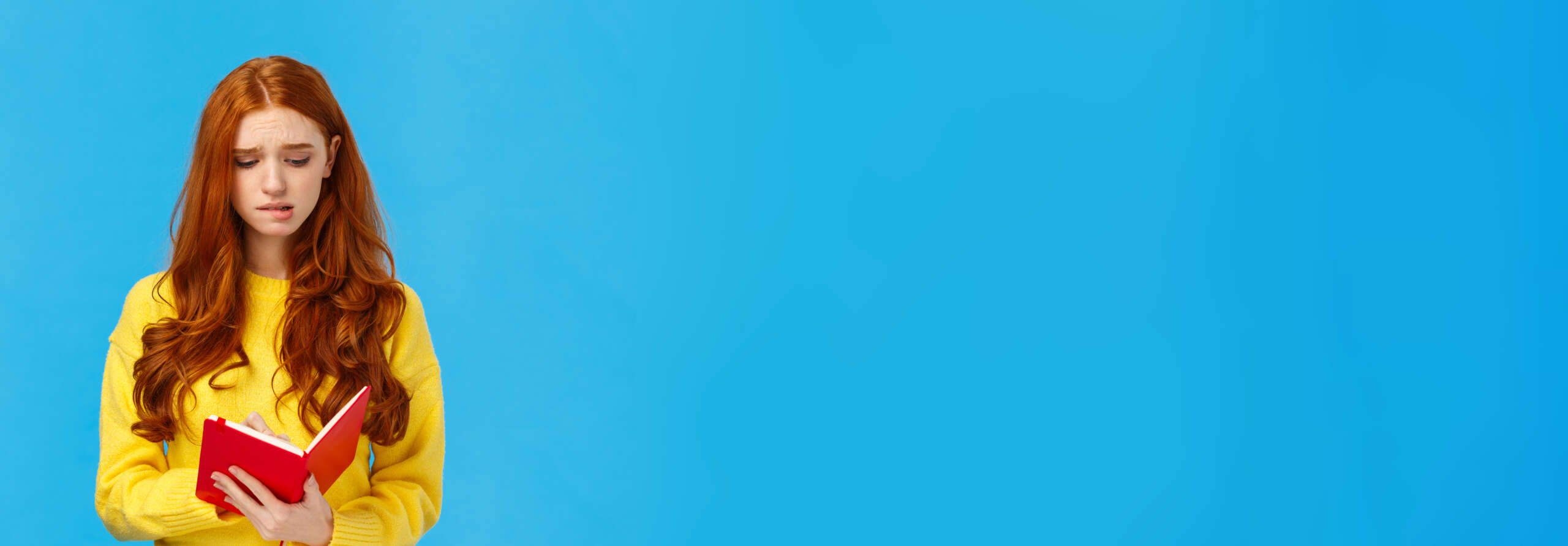 Perplexed and uneasy, concerned cute redhead female student having troubles with schedule, frowning reading girlfriend diary, feeling guilty, holding red notebook, feeling troubled, blue background